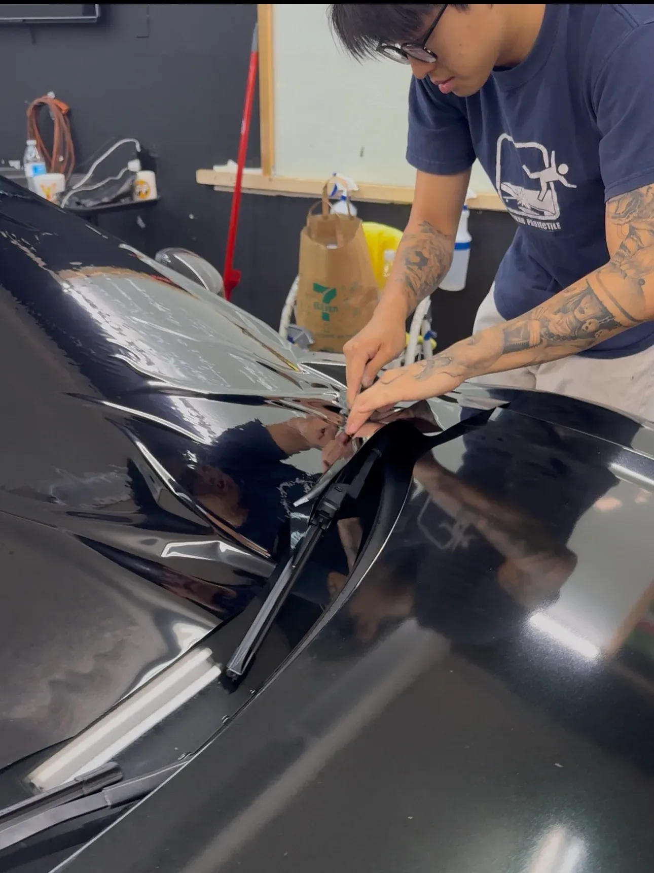 Paint protection film being floated across a dark hood before it is squeegeed down