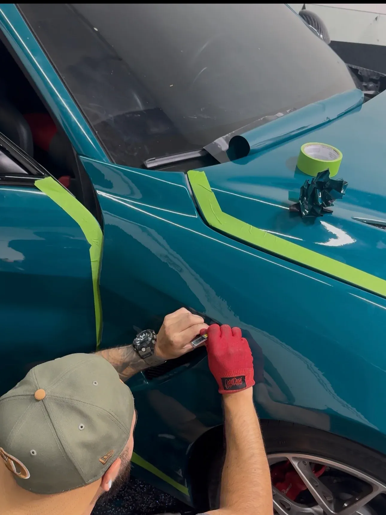 Film worked into the fender edge above the wheel arch, masking tape holding the run
