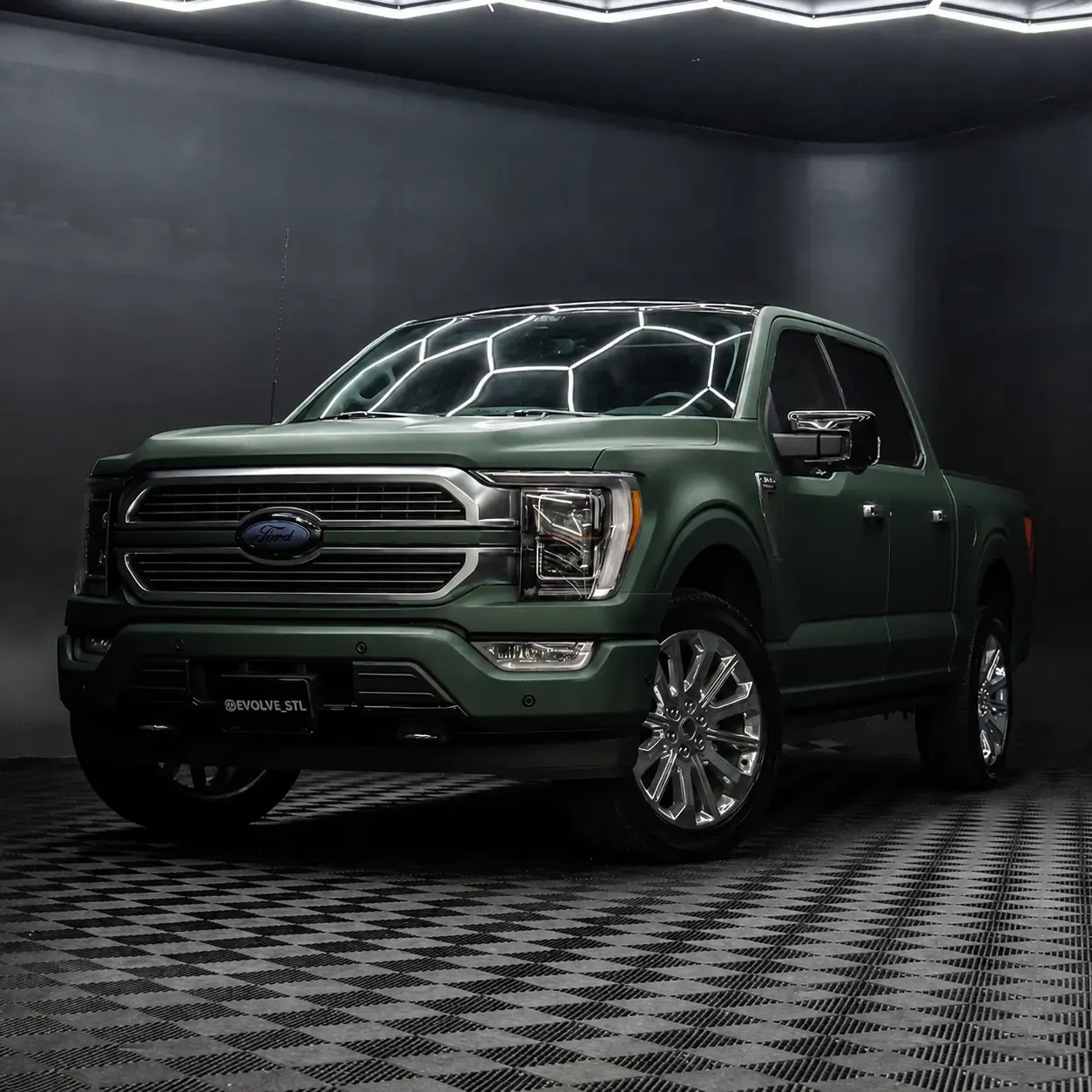 A crew-cab pickup in a matte green color-change wrap, lit in a studio bay